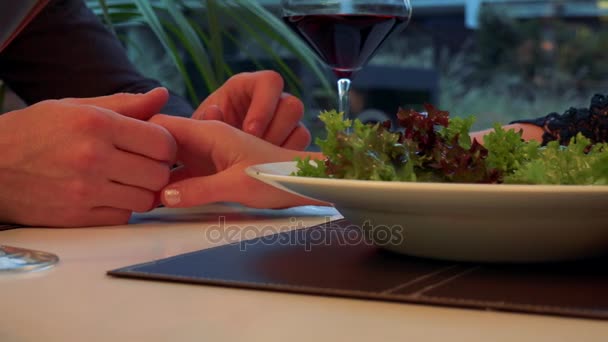 Mužské ruce držet a pohlazení ženské ruku přes stůl s jídlem a vínem - Záběry, video