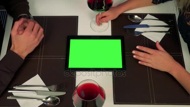 A man and a woman sit at a table (only hands are seen), a tablet with a green screen between them, the man explains something about it - Footage, Video
