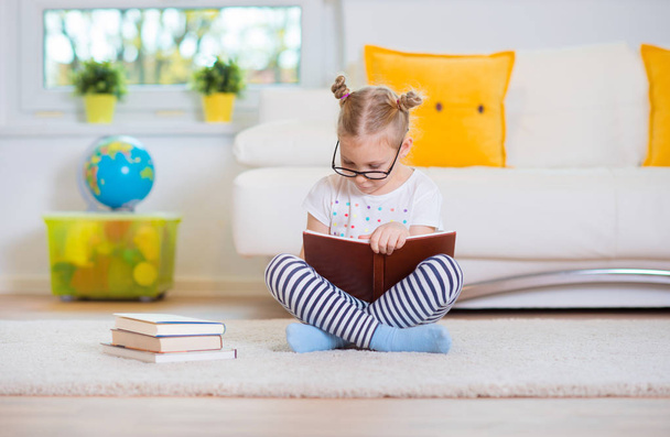 Retrato de menina esperta sentada com livro no chão
  - Foto, Imagem