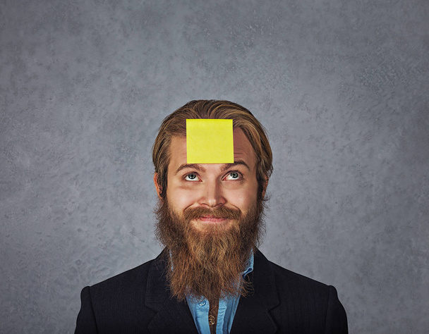 bearded smiling business man looking up to the sticker stick on his head forehead - Foto, imagen