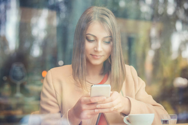 Happy girl using phone in coffee shop, through window view - Valokuva, kuva