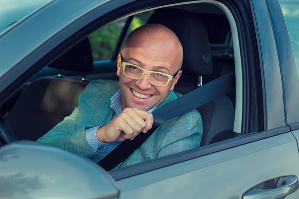 ハンサムな男が求める安全ベルトを締めることを示す彼の車でカメラを見て笑っています。安全な旅行の交通・車両のコンセプト. - 写真・画像