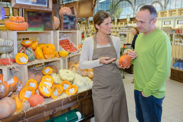 Shop assistant showing pumpkin to customer - 写真・画像