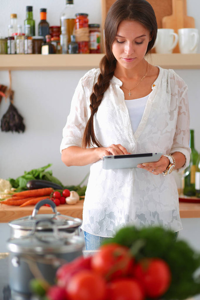 Молодая женщина использует планшетный компьютер, чтобы готовить на кухне - Фото, изображение