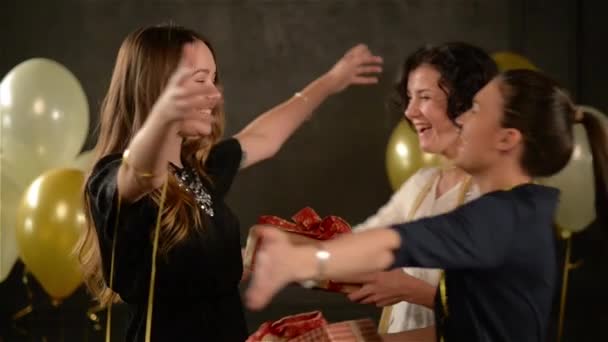 Twee opgewonden vrouwen gelukwensen met hun vriend haar knuffelen en het geven van een presenteert. Verjaardag meisje Recieved vakken met geschenken. Zwarte achtergrond met witte en gouden lucht ballonnen. - Video