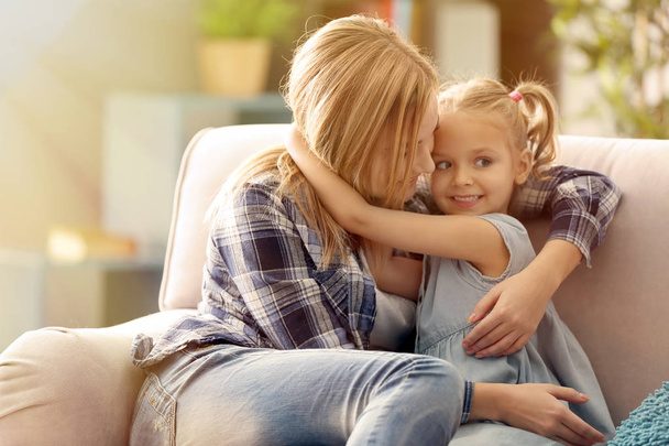 Kaunis nuori nainen ja hänen tyttärensä istuu sohvalla kotona. Äitienpäivän käsite
 - Valokuva, kuva