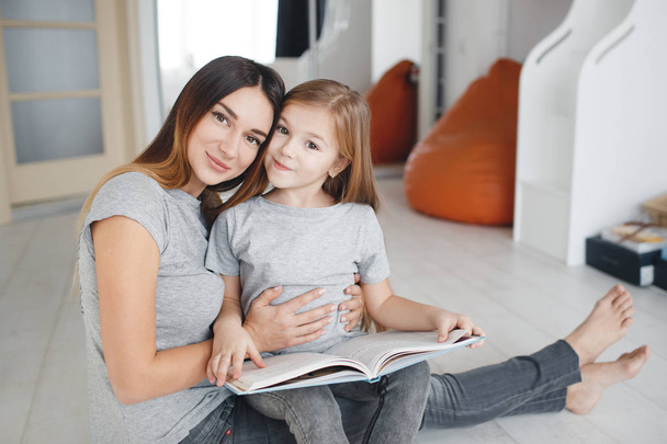Mother and daughter reading a book sitting on the floor - Фото, зображення