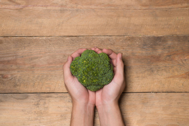 Fresh broccoli in hands on a wooden background - Foto, Imagem
