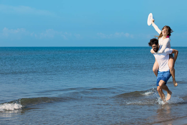 A guy carrying a girl on back at beach - Фото, зображення
