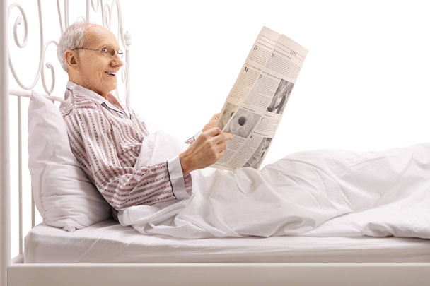 Mature man lying in bed and reading a newspaper - Photo, Image