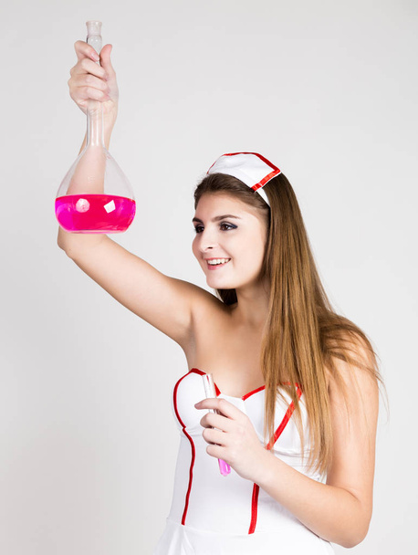 Beautiful smiling sexy nurse standing and holding test tube with pink liquid - Photo, image