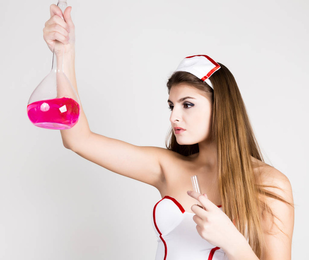 Beautiful smiling sexy nurse standing and holding test tube with pink liquid - Foto, afbeelding
