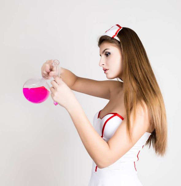 Beautiful smiling sexy nurse standing and holding test tube with pink liquid - Foto, afbeelding