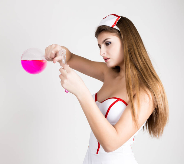 Beautiful smiling sexy nurse standing and holding test tube with pink liquid - Foto, imagen