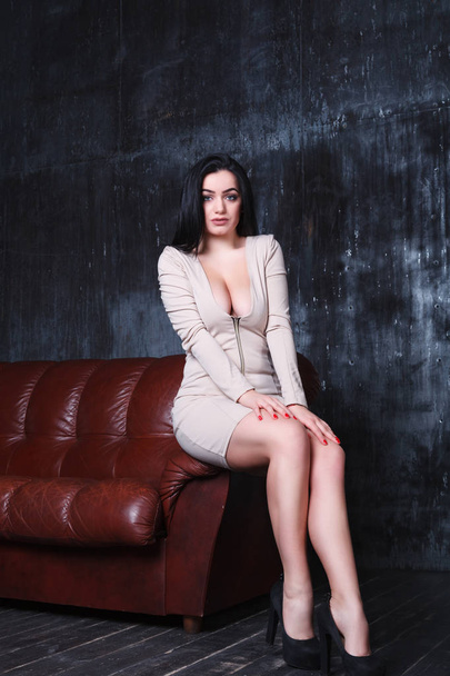 Beautiful woman in an elegant dress, standing beside the couch - Fotó, kép