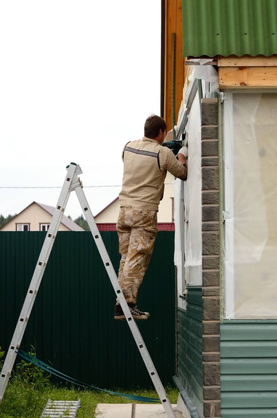 Чоловік професійний працівник стоїть на драбині, займається оздобленням домашнього сайдингу
 - Фото, зображення
