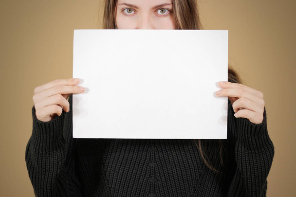 Girl holding white A4 blank paper. Covers the face, mouth and no - Fotografie, Obrázek
