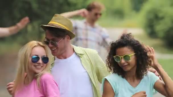 Roztomilý kluk tancuje s dvěma náhodných dívek na venkovní párty, ruce na jejich pasu - Záběry, video