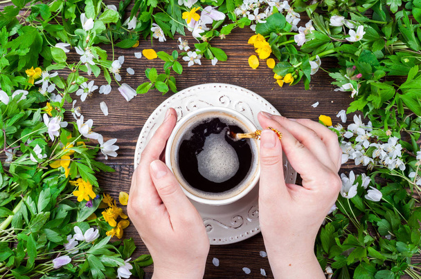 Csésze kávé tartó női kezek. Tavasszal. Virágok és a kávé, a rusztikus, fából készült háttér - Fotó, kép