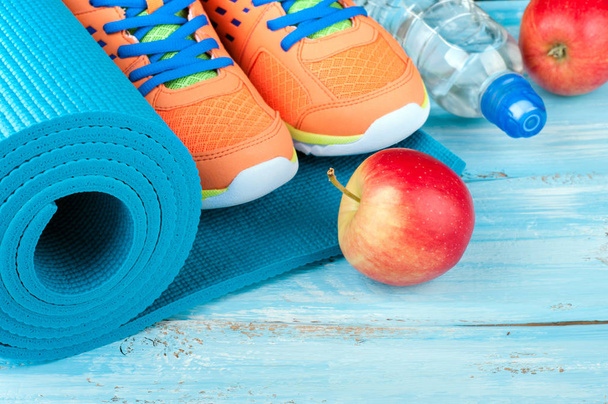 Tapete de ioga, sapatos esportivos, maçã, garrafa de água no fundo de madeira azul. Conceito de estilo de vida saudável, alimentação saudável, esporte e dieta. Equipamento desportivo
 - Foto, Imagem