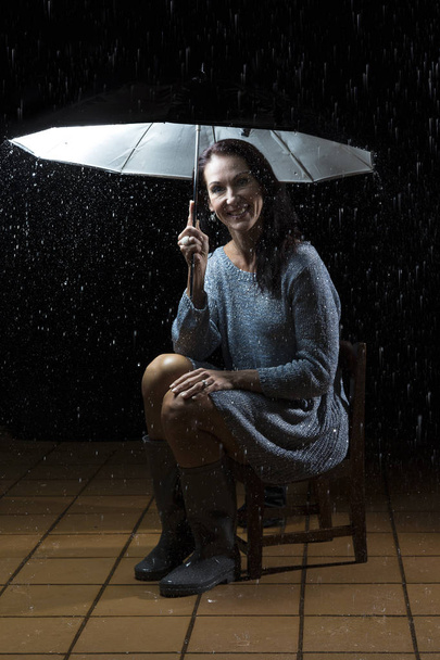 Beautiful woman with silver dress sitting under an umbrella at n - Zdjęcie, obraz