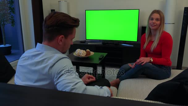 Egy férfi és egy nő, egy díványon, a nappaliban egy komoly ügy - egy zöld képernyő, a háttérben egy Tv megvitatása - Felvétel, videó
