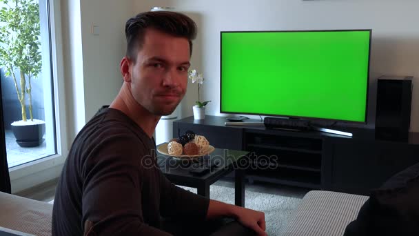 Un hombre joven y guapo ve un televisor con una pantalla verde, luego se gira hacia la cámara y sacude la cabeza, infeliz
 - Metraje, vídeo