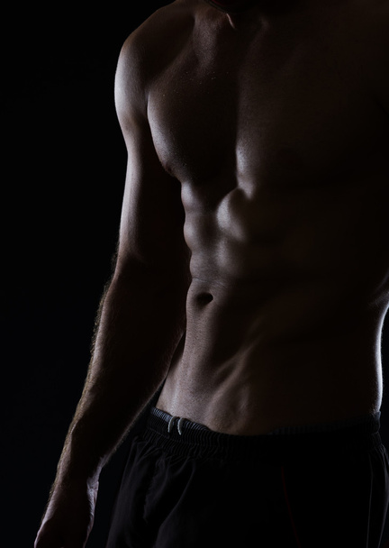 Closeup on muscular male torso with abdominal muscles on black - Fotoğraf, Görsel