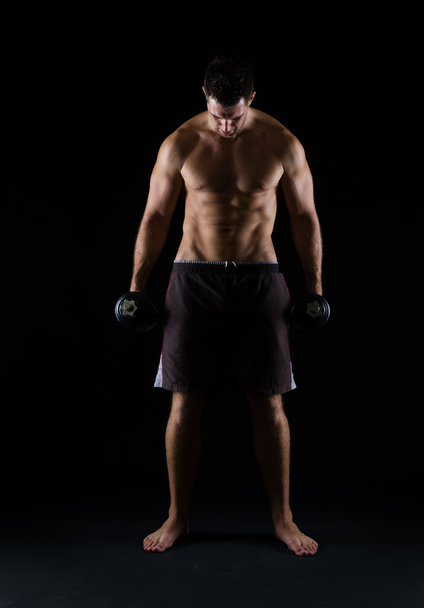 Strong muscular man holding dumbbell on black - Фото, зображення