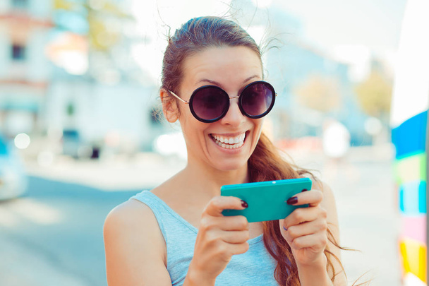 Happy woman holding smartphone smiling celebrating his success over city scape background - Фото, изображение