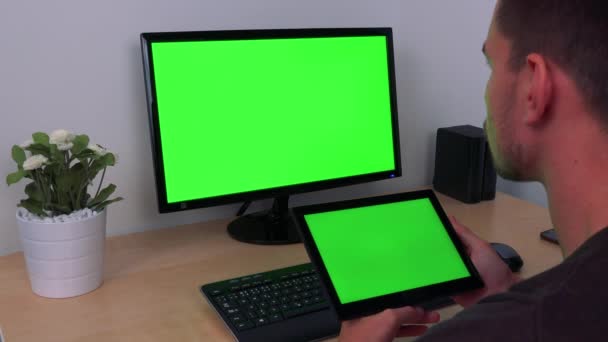 ein Mann beobachtet abwechselnd sein Tablet und einen Computerbildschirm, beide grüne Bildschirme - Filmmaterial, Video