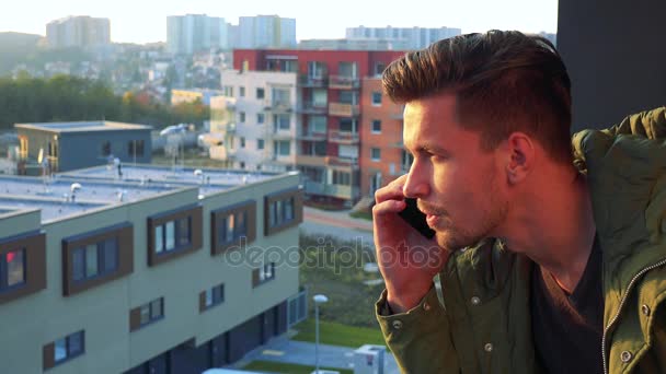 Bir balkon bir smartphone cep telefonu ile bir genç, yakışıklı bir adam görüşmeler - Video, Çekim