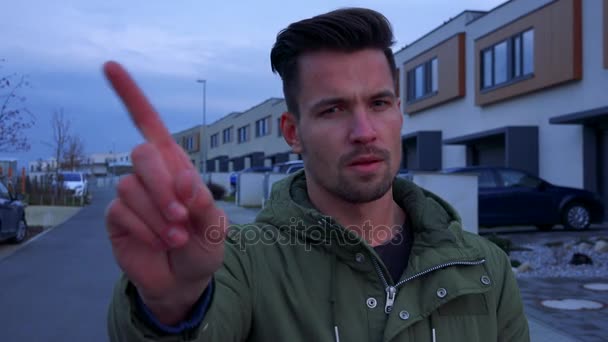 ein junger, gutaussehender Mann steht auf einer Straße in einer Nachbarschaft und schüttelt zum Zeichen der Missbilligung den Finger - Filmmaterial, Video