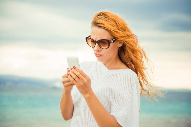 skeptical serious woman texting on phone displeased with conversation sea ocean outdoors background  - Фото, изображение