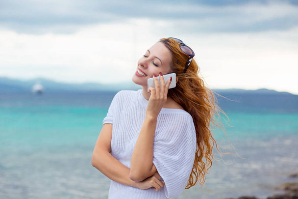 young happy woman talking on mobile phone on a beach with ocean sea background, Sardinia Italy  - Zdjęcie, obraz