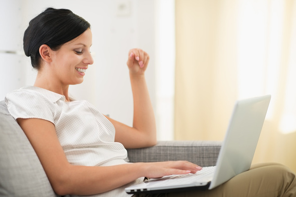 Happy young woman using laptop in living room - Foto, imagen