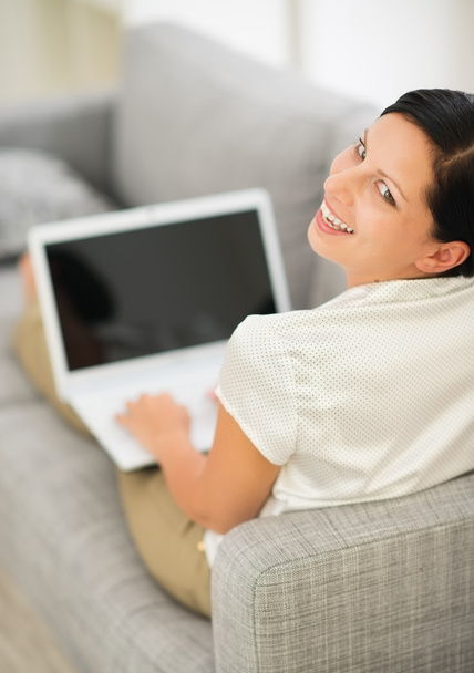 Smiling young woman laying on couch and using laptop - Foto, Imagem