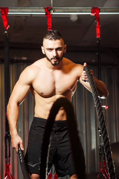 Young fit man exercising with battle ropes in the fitness gym - Fotó, kép