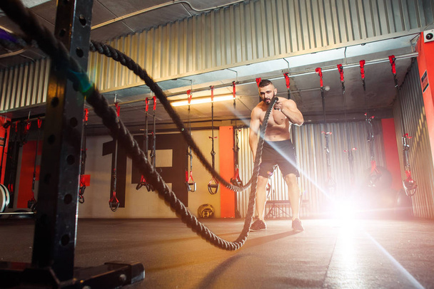 Joven hombre en forma haciendo ejercicio con cuerdas de batalla en el gimnasio de fitness
 - Foto, imagen