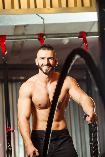 Young fit man exercising with battle ropes in the fitness gym - Фото, зображення