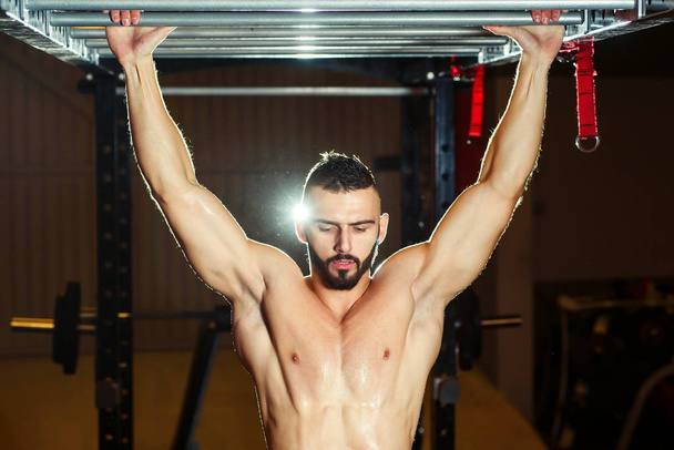 Athlete muscular fit man pulling up on horizontal bar in a gym - Фото, зображення