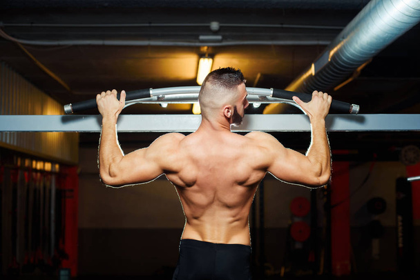 Athlete muscular fit man pulling up on horizontal bar in a gym - Foto, Bild