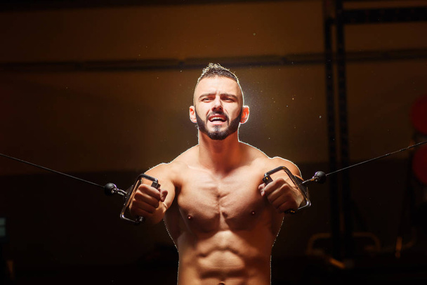 Young athletic tired man with beard pumping up muscles on crosso - Photo, image