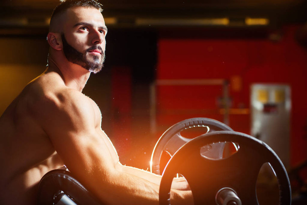 Young muscular man training biceps with barbells in gym - Φωτογραφία, εικόνα