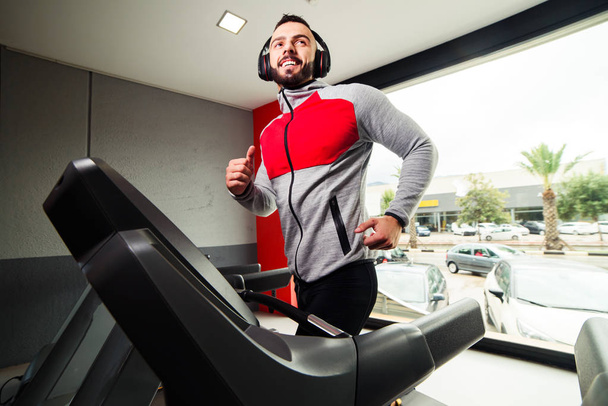 Smiling man with earphones exercising on treadmill in gym - Photo, Image