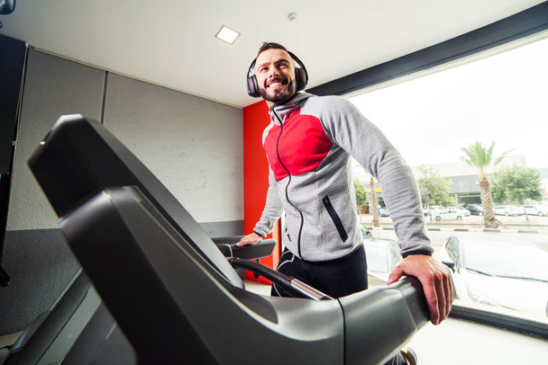 Smiling man with earphones exercising on treadmill in gym - Foto, Bild