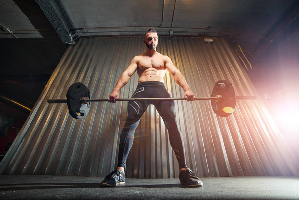 Muscular young man making deadlift with barbells at gym - Photo, image