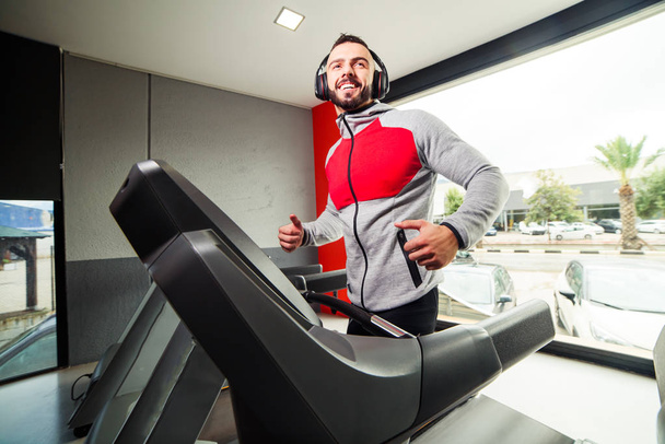 Smiling man with earphones exercising on treadmill in gym - Фото, изображение
