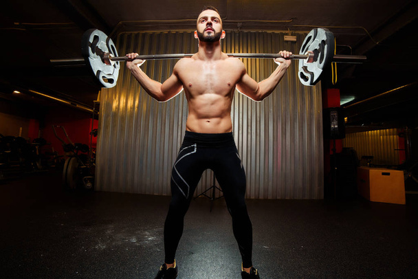 Muscular man training squats with barbells at gym - Foto, afbeelding