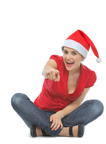 Happy woman in Santa hat sitting on floor and pointing in camera - Fotoğraf, Görsel